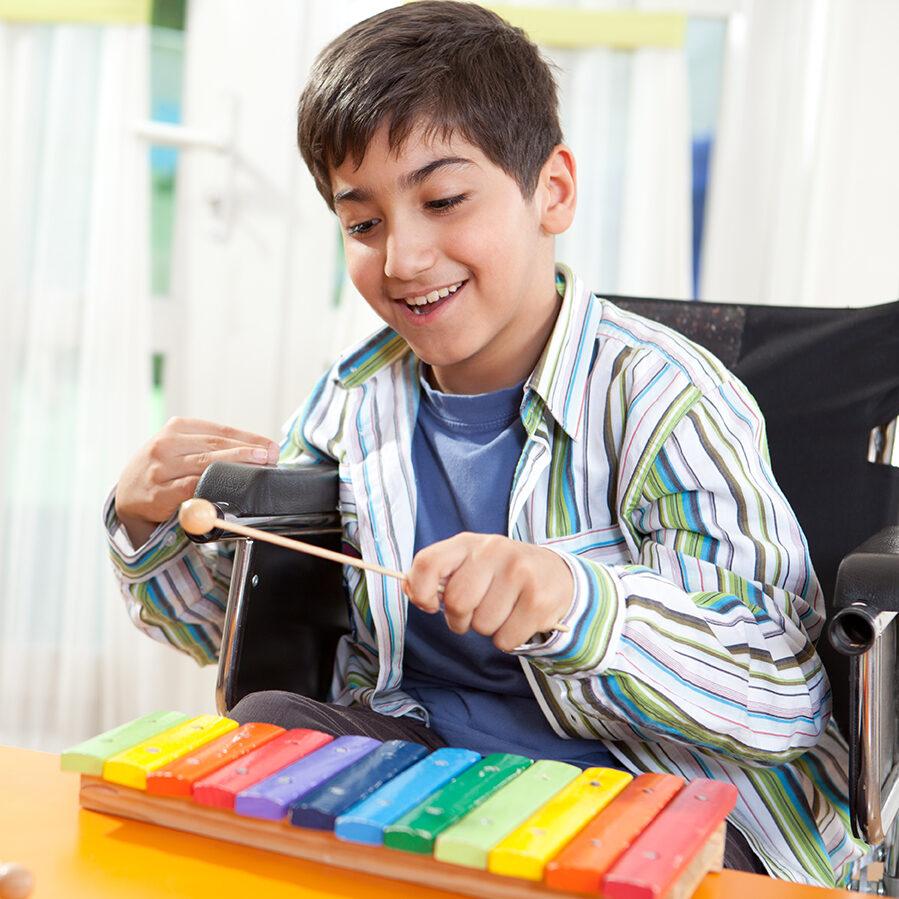 Little boy in wheelchair playing musical instrument.